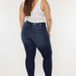 Woman modeling high waisted raw hem jeans in dark blue with a white tank top and heels, showing back view