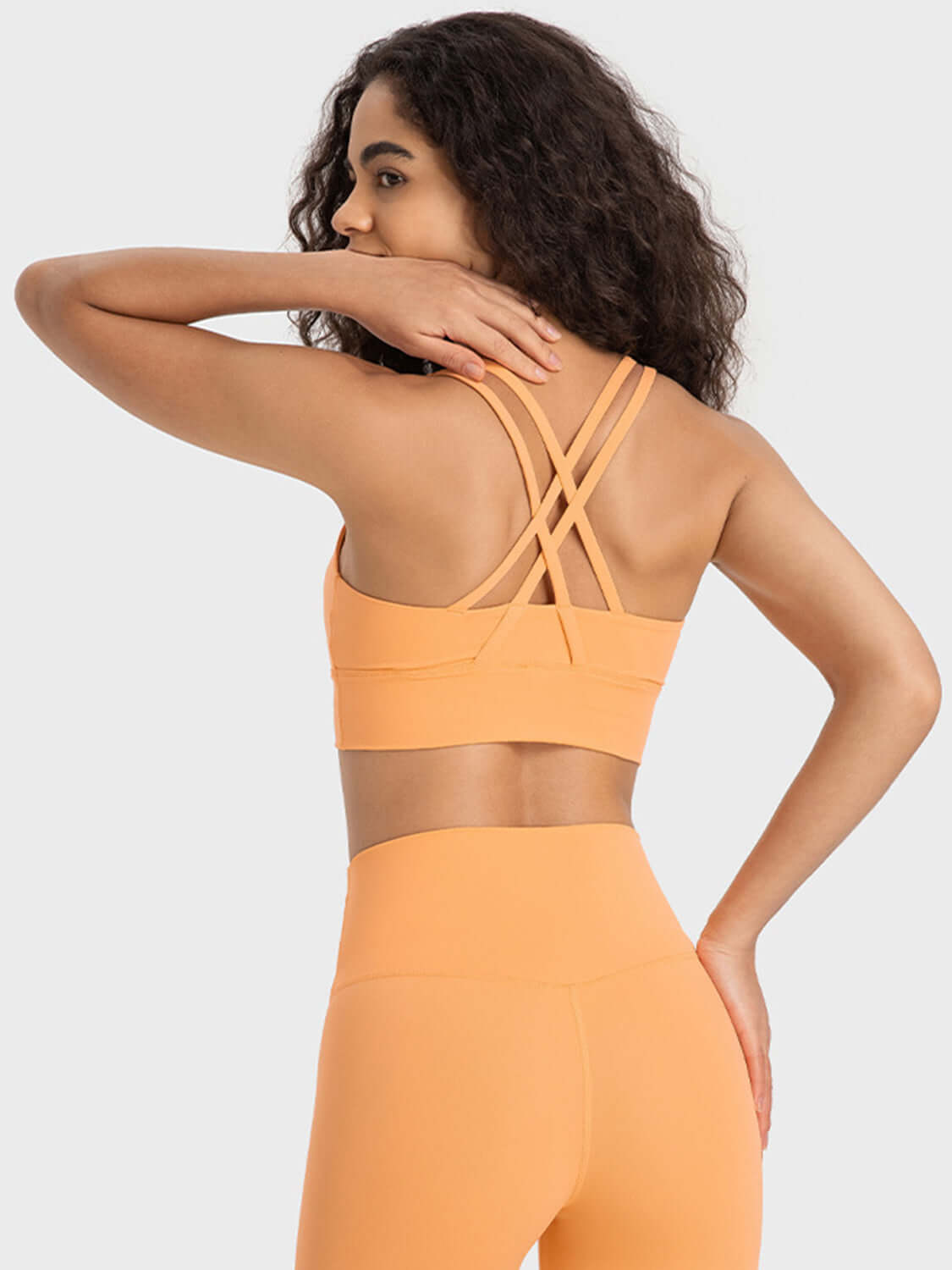 Woman in orange crisscross active tank showcasing stylish back design, ideal for workouts and comfort.