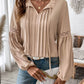 Woman wearing Perfee Frill Tie Neck Long Sleeve Blouse in beige with delicate ruffled details and lace sleeves, holding a white clutch.