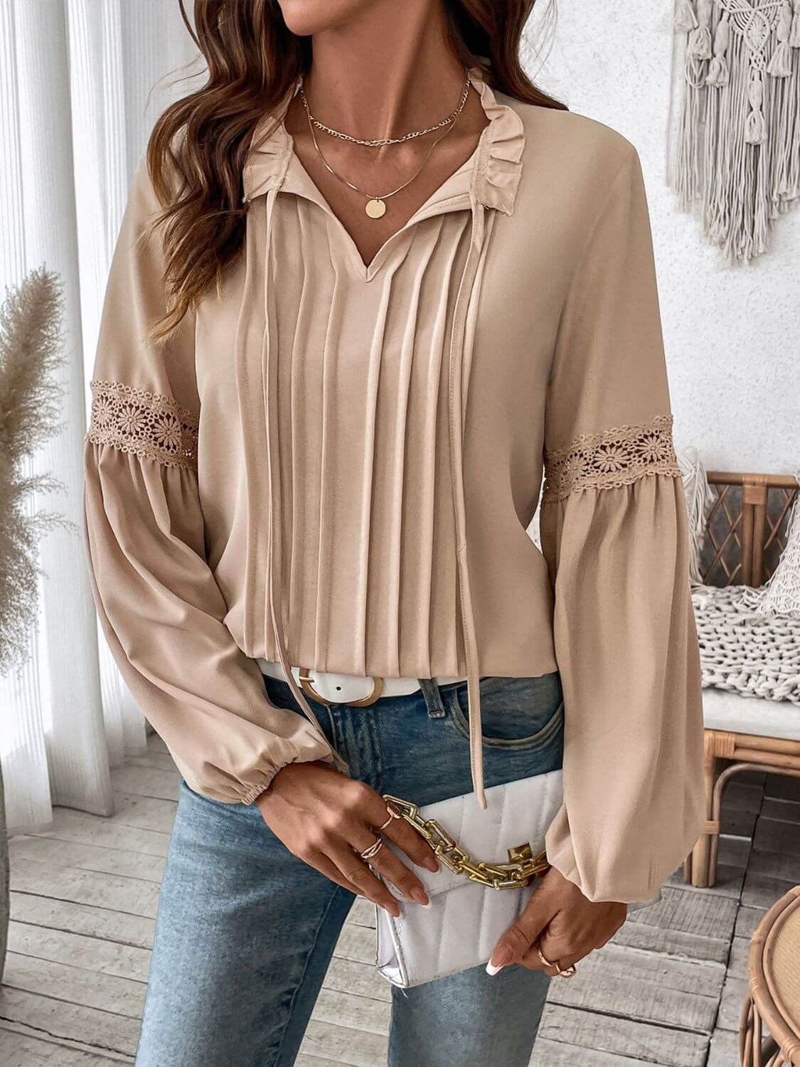 Woman wearing Perfee Frill Tie Neck Long Sleeve Blouse in beige with delicate ruffled details and lace sleeves, holding a white clutch.