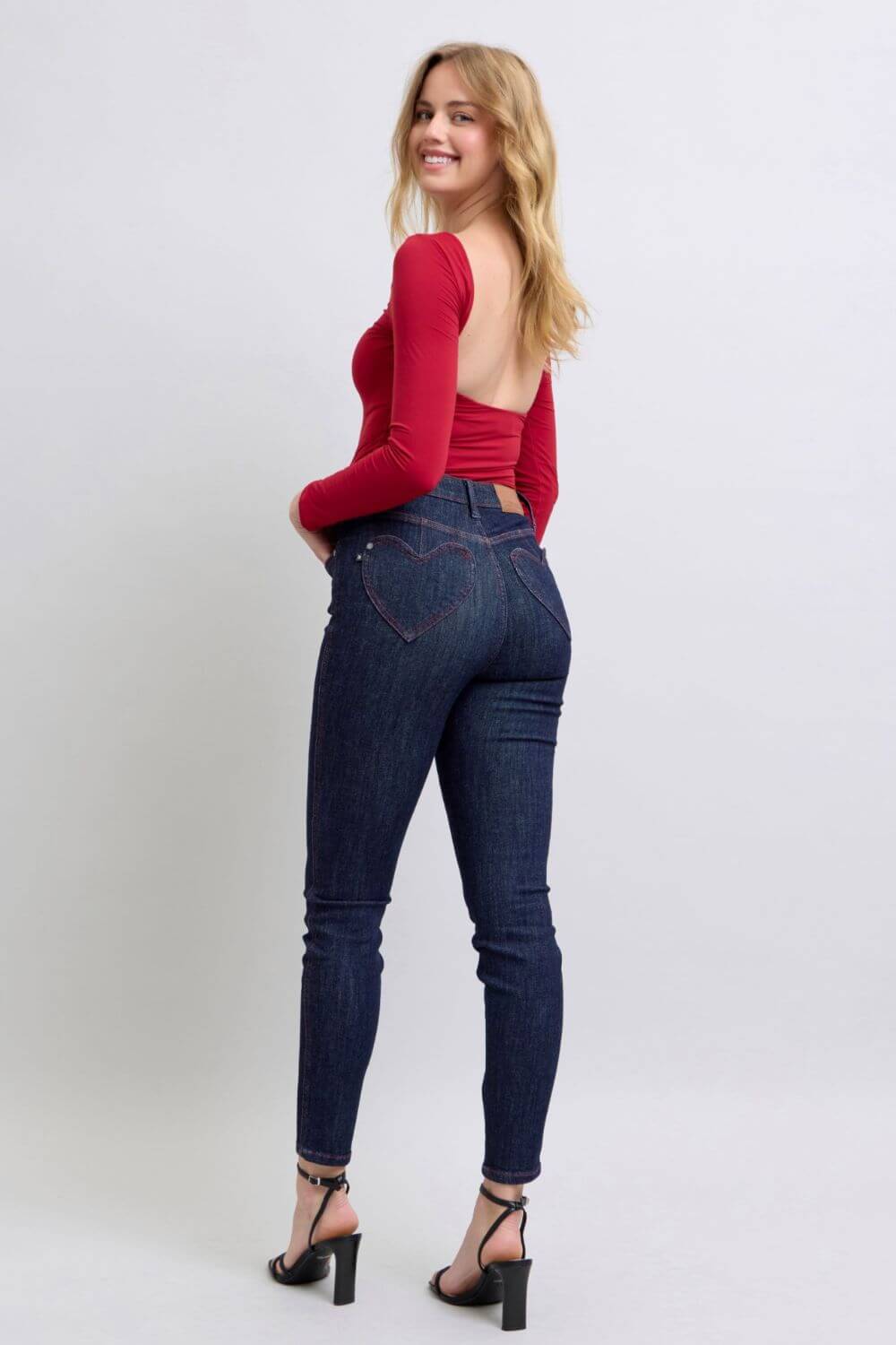 Woman in red top wearing Judy Blue Heart Shaped Back Pockets Skinny Jeans, showcasing stylish back pocket detail.