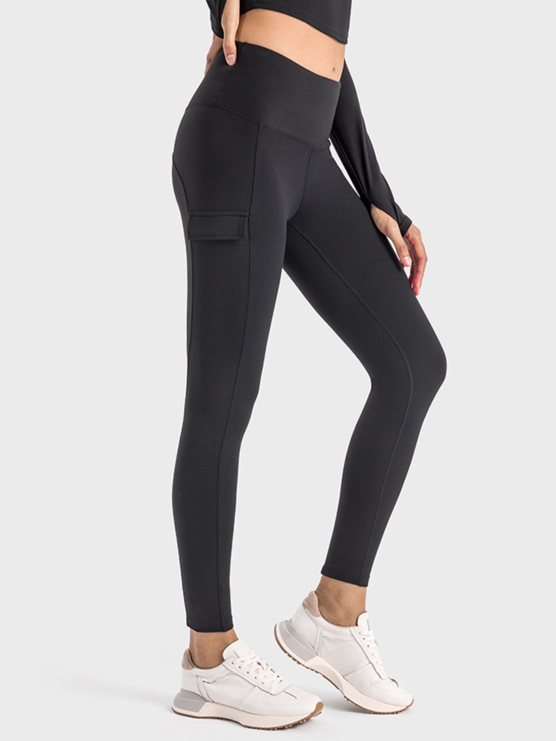 Millennia wide waistband sports leggings with pocket, modeled in black, paired with white sneakers for an active look.