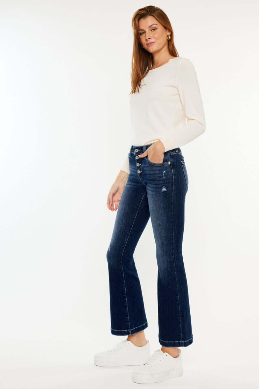 Woman wearing Kancan mid-rise button fly flare jeans with white top and sneakers.