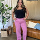 Woman wearing RFM Full Size High Rise Garment Dye Wide Leg Jeans in pink, standing in a stylish, modern living room.