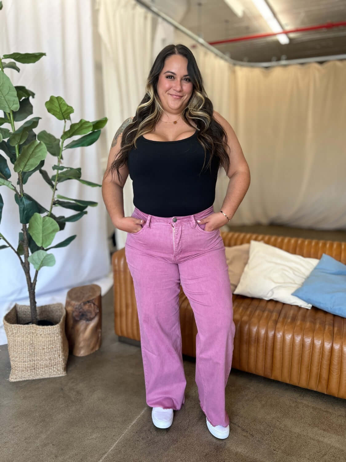 Woman wearing RFM Full Size High Rise Garment Dye Wide Leg Jeans in pink, standing in a stylish, modern living room.