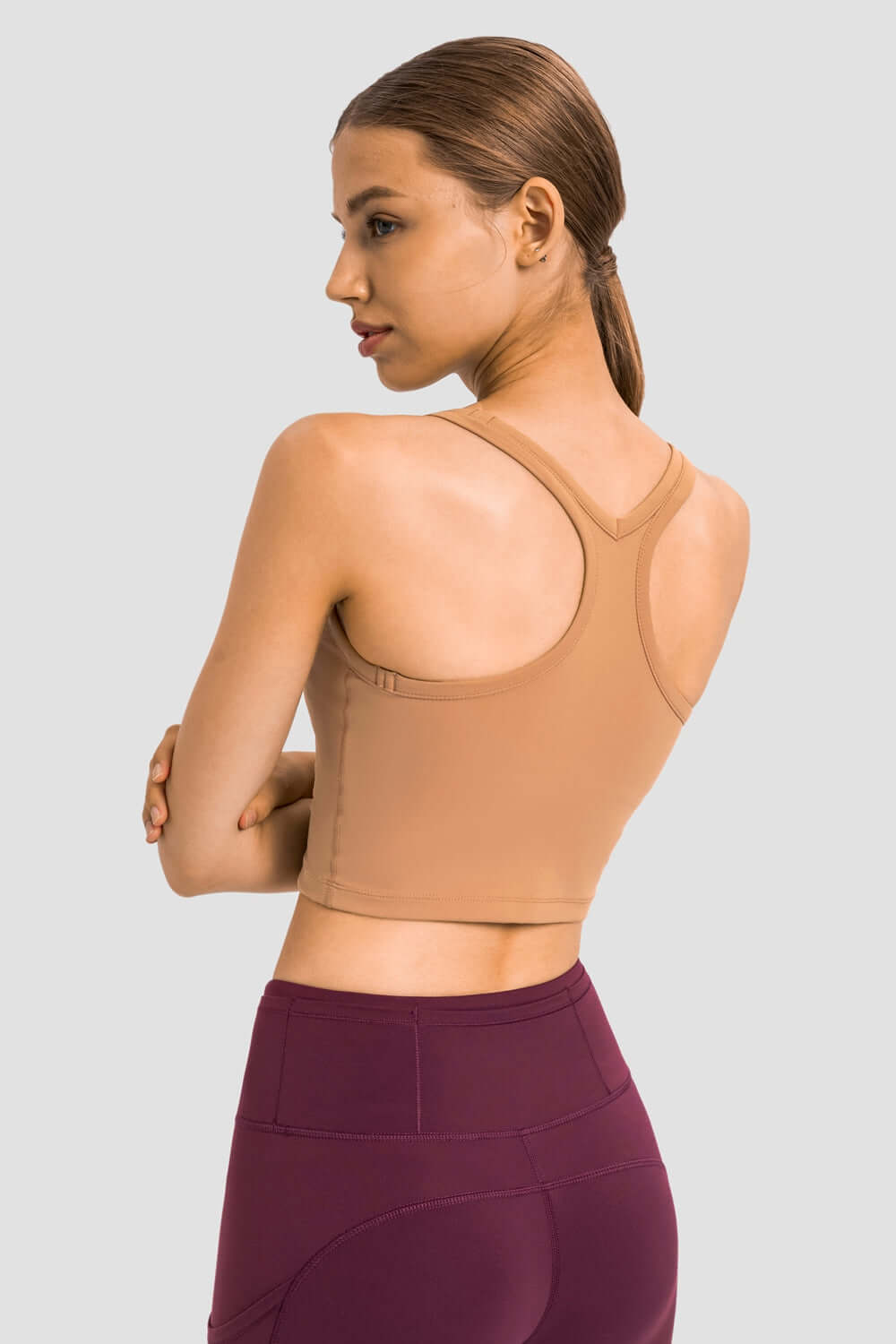 Back view of a woman wearing a Millennia Racerback Sports Bra in a tan color, showcasing its sleek design and sporty style.