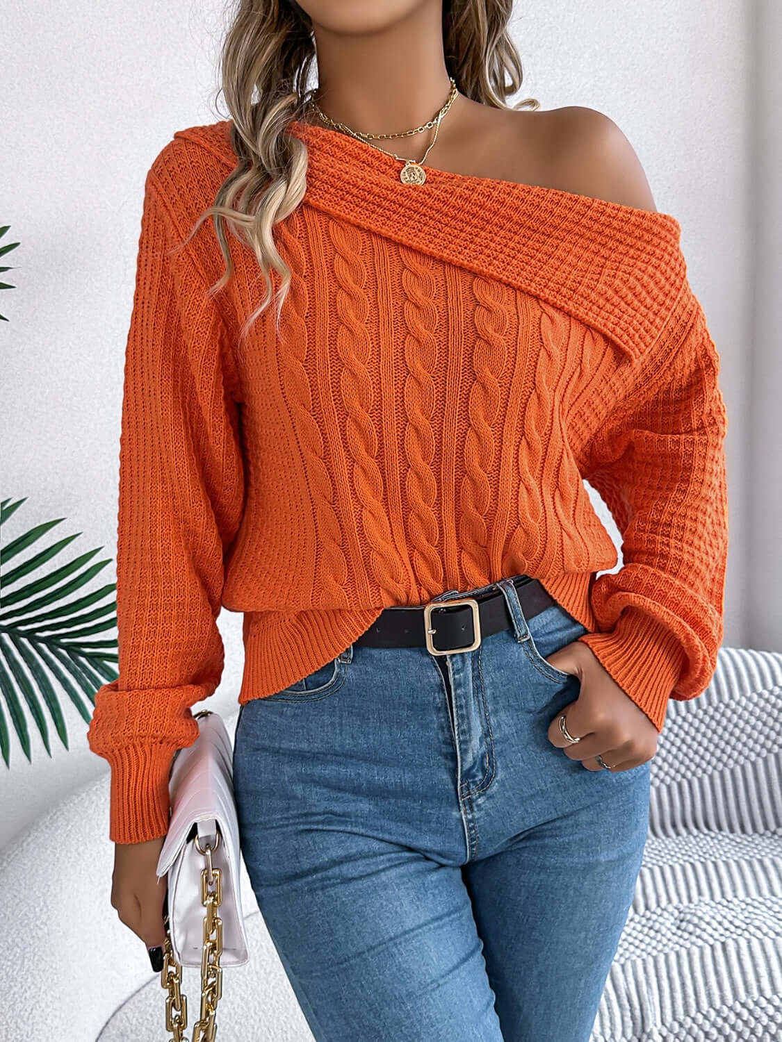 Woman wearing Bella Road Cable-Knit One Shoulder Long Sleeve Sweater in orange, paired with jeans and belt.