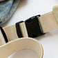 Close-up of black buckle and beige strap on a crossbody bag, with denim fabric in the background.