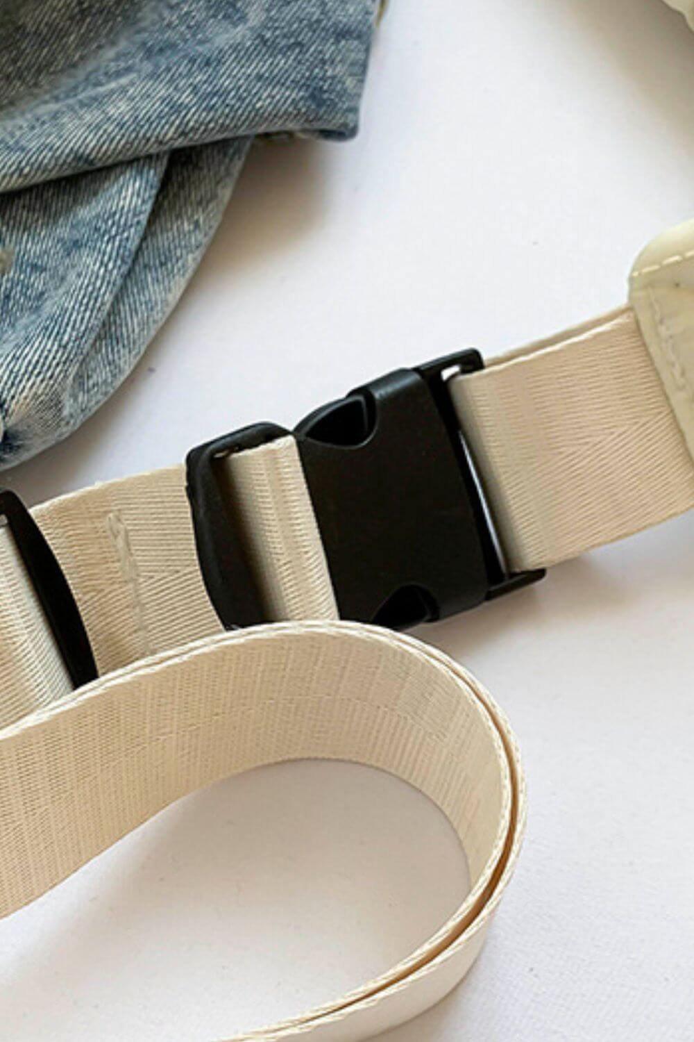 Close-up of black buckle and beige strap on a crossbody bag, with denim fabric in the background.