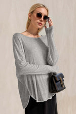 Woman wearing a stylish gray high-low long sleeve T-shirt with sunglasses and a chic bag, exuding a cool and relaxed vibe.