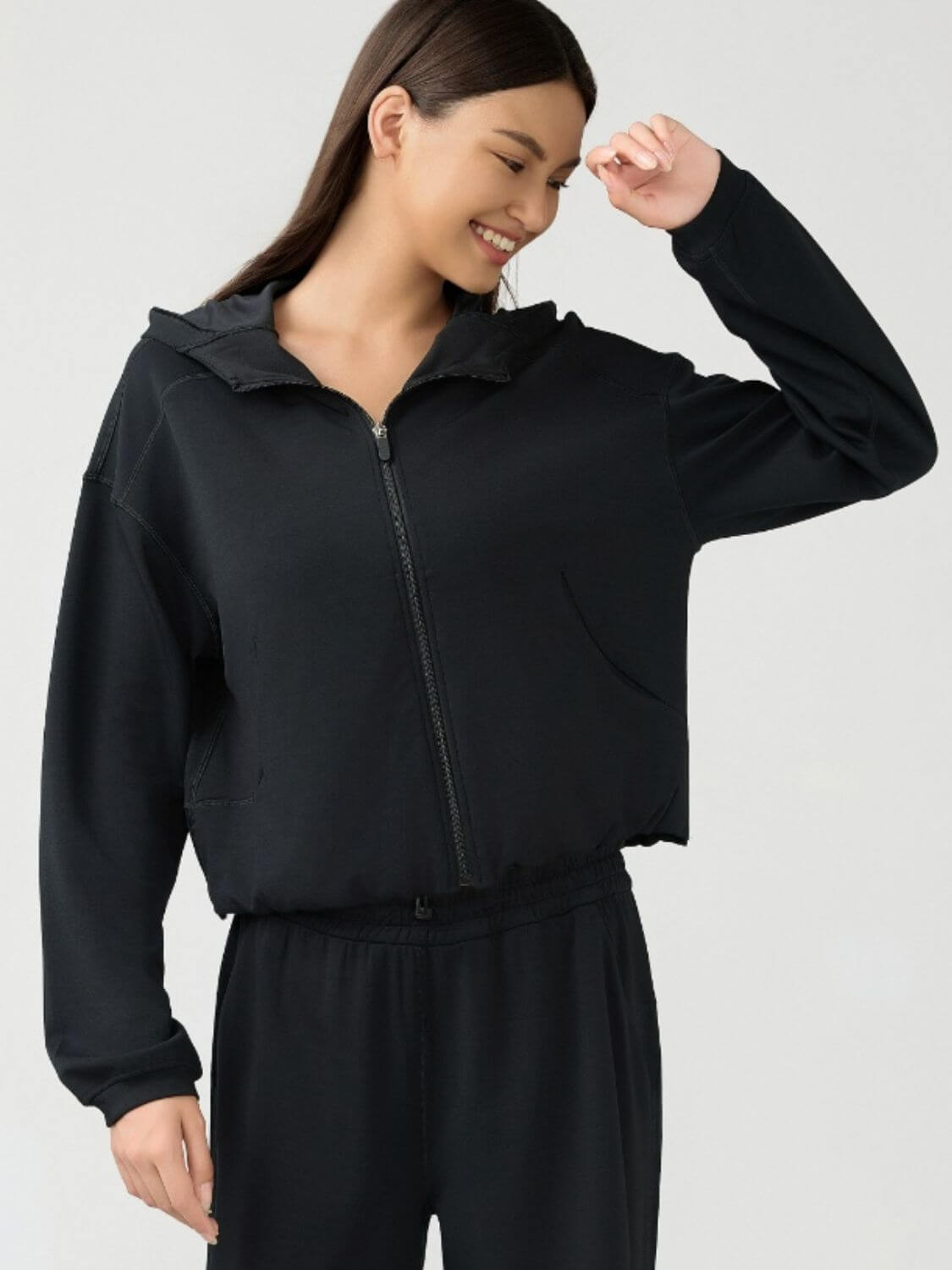 Stylish woman in a black Millennia zip-up hoodie with dropped shoulders, perfect for an active lifestyle and comfortable workouts.