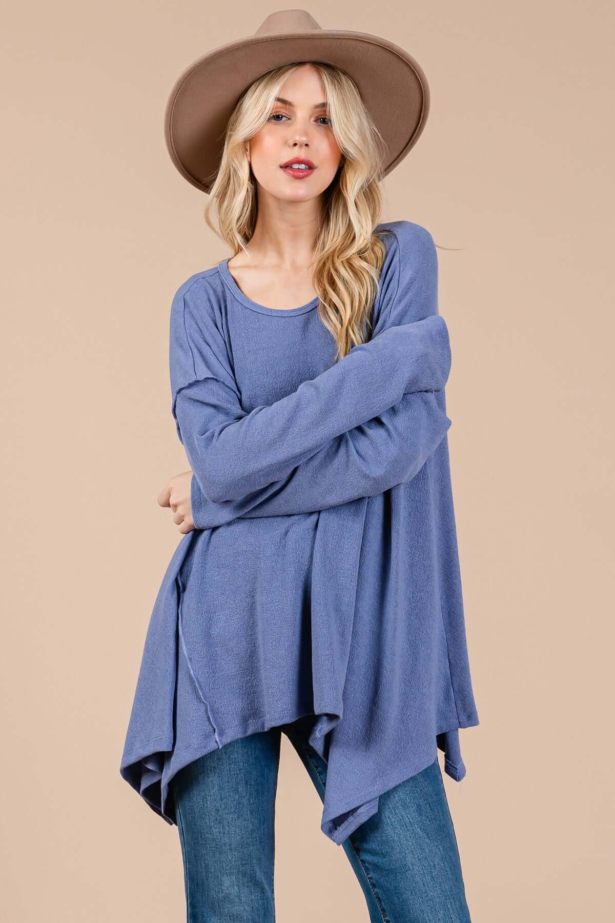 Woman wearing Ces Femme asymmetrical long sleeve top in blue with a hat, showcasing drop sleeves and a relaxed fit.