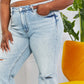 Woman wearing high-waisted light wash distressed dad jeans with cat's whiskers fading and raw hem paired with white crop top.