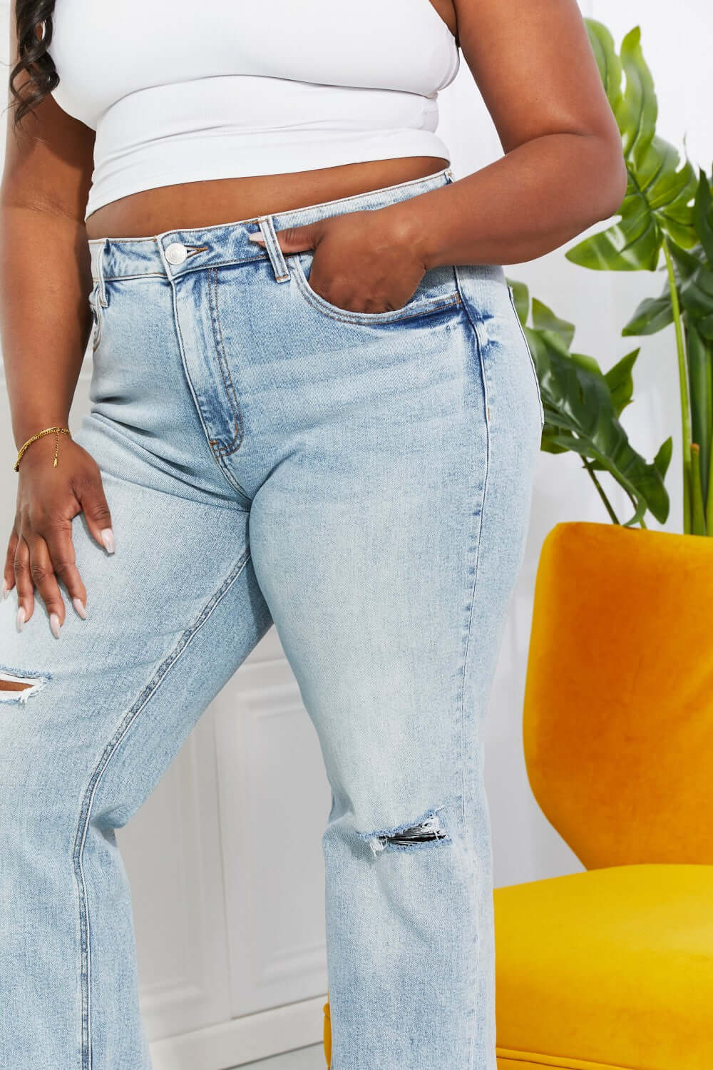 Woman wearing high-waisted light wash distressed dad jeans with cat's whiskers fading and raw hem paired with white crop top.