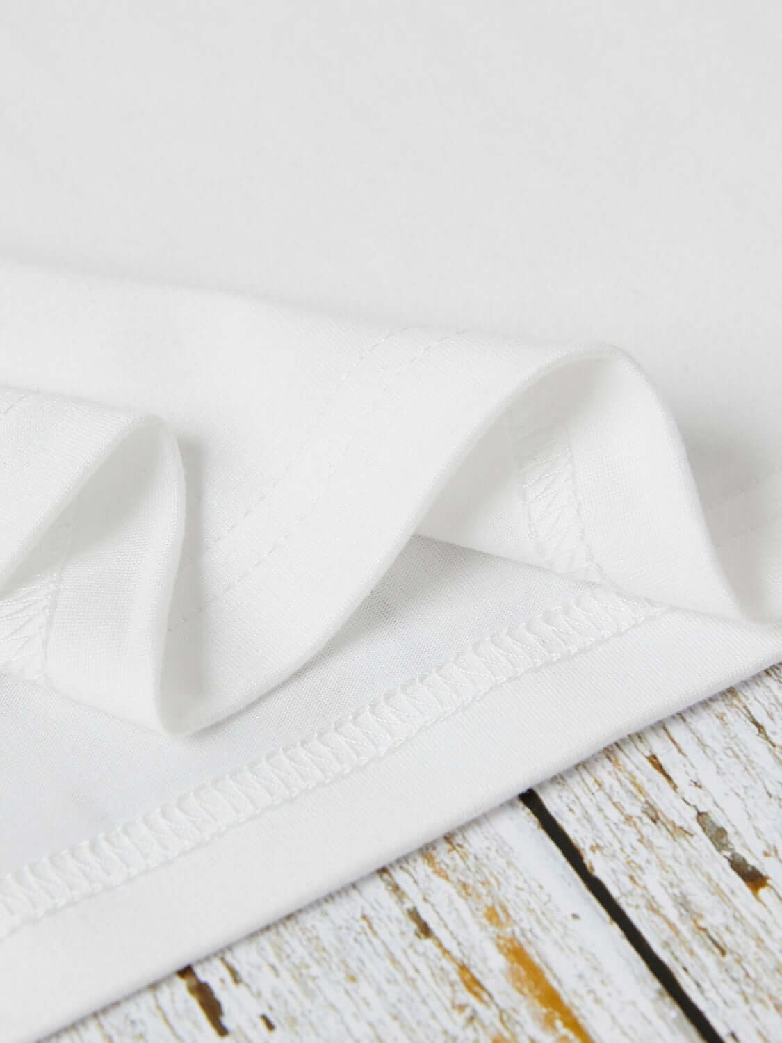 Close-up of the hem and stitching on a white graphic round neck short sleeve T-shirt made of 100% polyester.