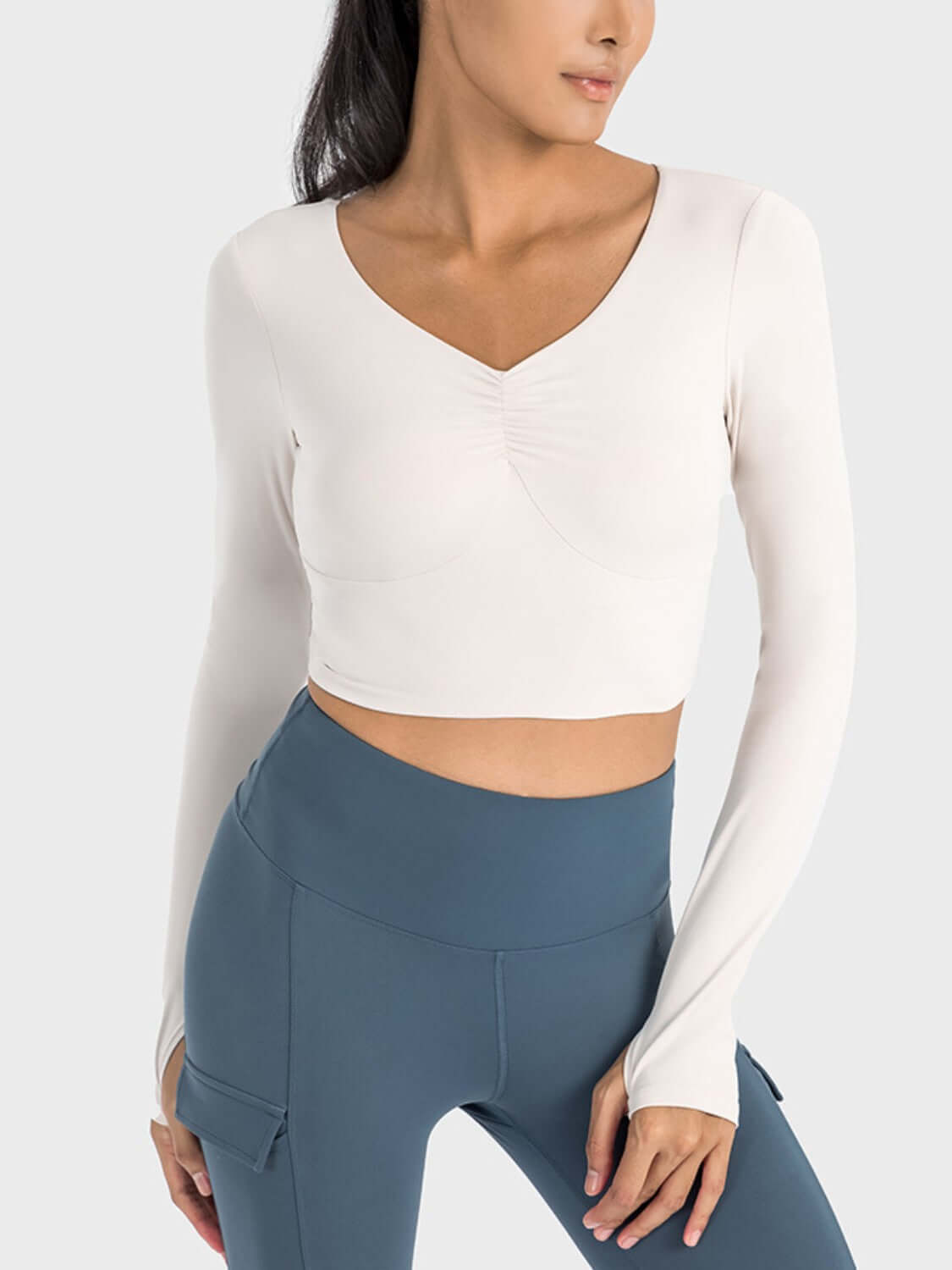 Millennia Ruched Cropped Long Sleeve Sports Top in cream, paired with stylish high-waisted leggings for an active look.