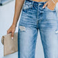 Woman wearing distressed straight leg jeans with hand in pocket, holding a beige clutch bag.