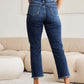 Woman wearing RFM Jeans Crop Dylan Full Size Tummy Control Distressed High Waist Raw Hem Jeans standing in a modern living room.