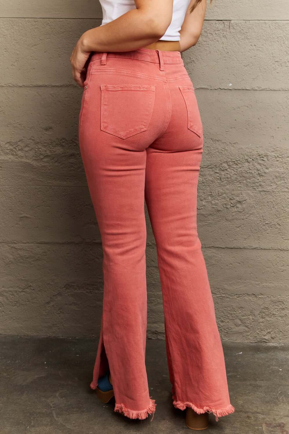 Woman wearing Bailey High Waist Side Slit Flare Jeans in pink by Risen Jeans, showcasing back view with side slit and frayed hem.