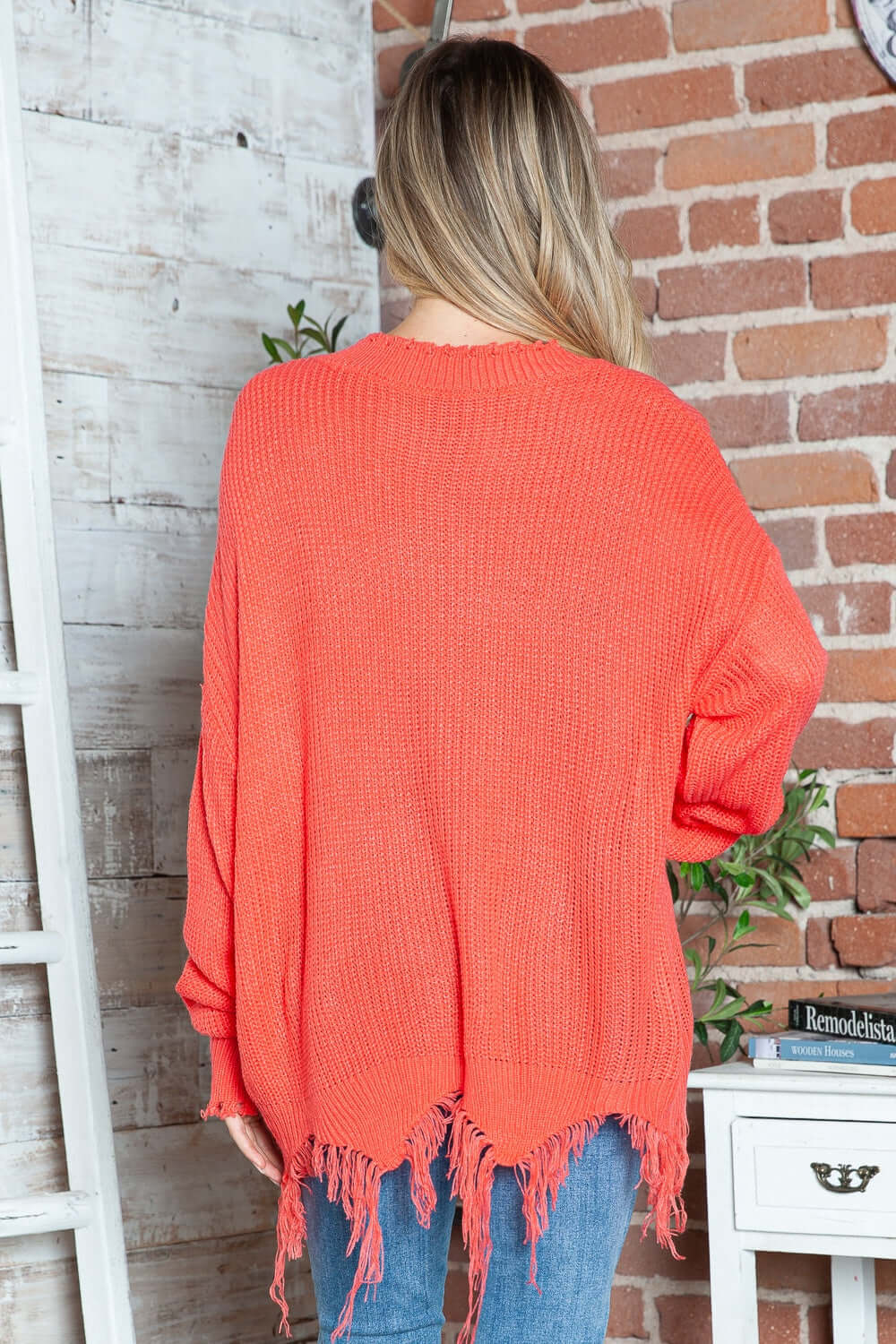 Woman wearing Bella Road Frayed Hem Sweater in vibrant orange, showcasing dropped shoulder style and playful frayed details.