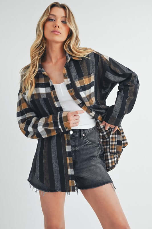 Stylish model showcases Aem+Co curved hem plaid button-up shirt layered over a white tank and black shorts.