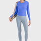 Woman in blue long sleeve sports top and gray leggings, ready for a workout with a yoga mat bag.