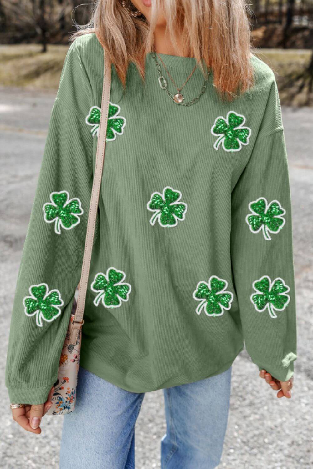 Stylish woman wearing a green long sleeve sweatshirt with sparkling sequin clovers, perfect for casual outings.