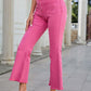 Woman wearing Bella Road Raw Hem High Waist Bootcut Jeans in pink with a white crop top and white heeled sandals standing outside.