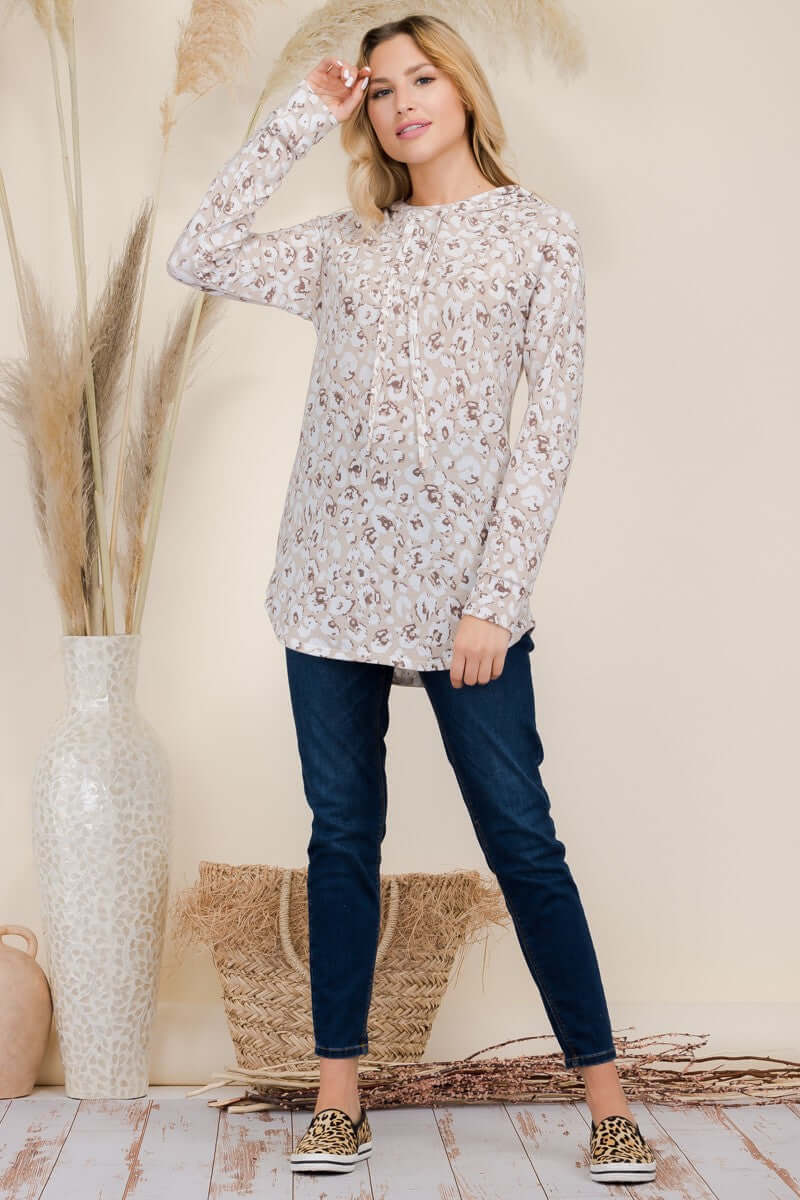 Woman in long sleeve leopard blouse with drawstring, paired with dark jeans and stylish sneakers, standing against a neutral background.