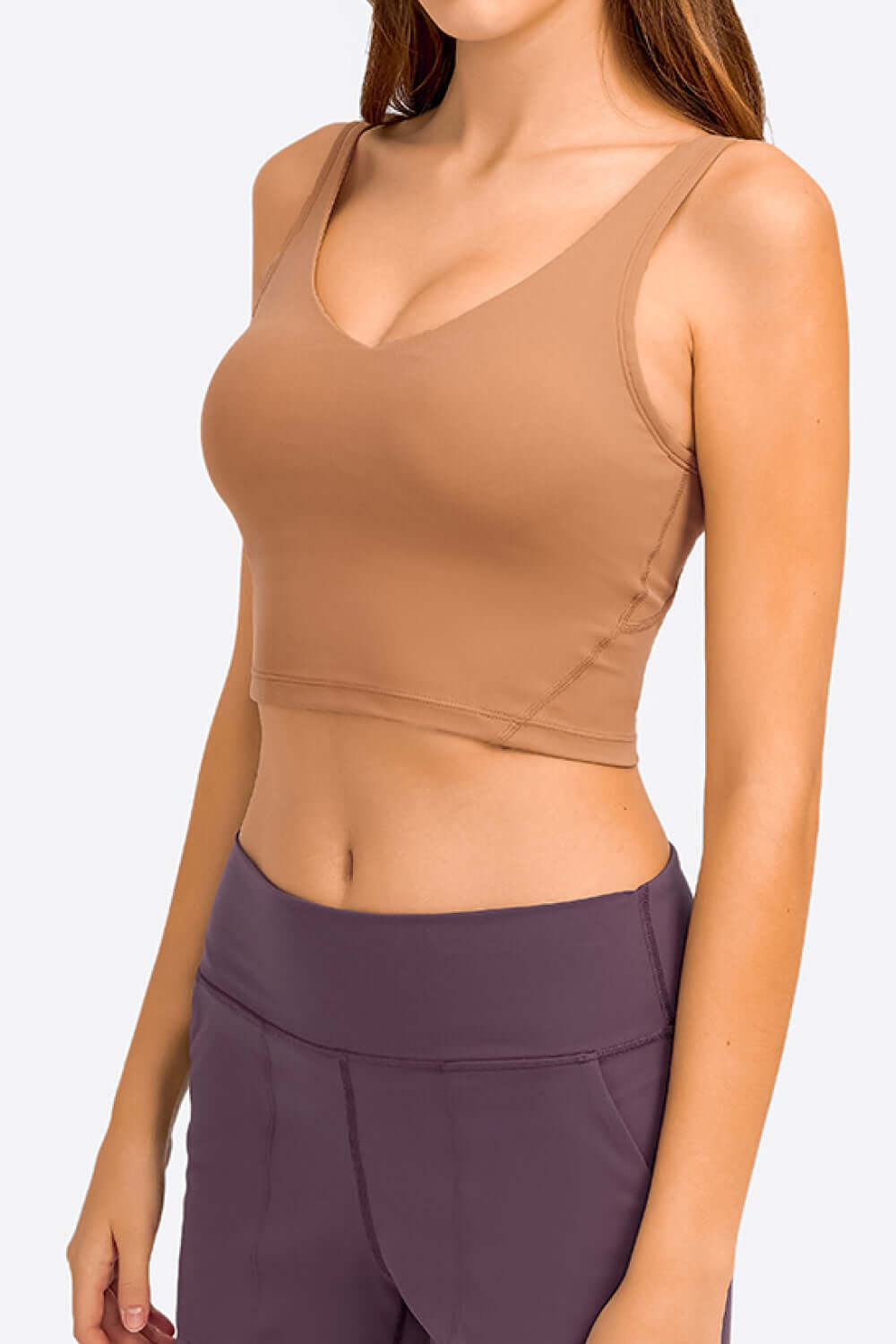 Model wearing Millennia Deep V-Neck Crop Sports Bra in warm brown, showcasing its stylish design and comfortable fit.