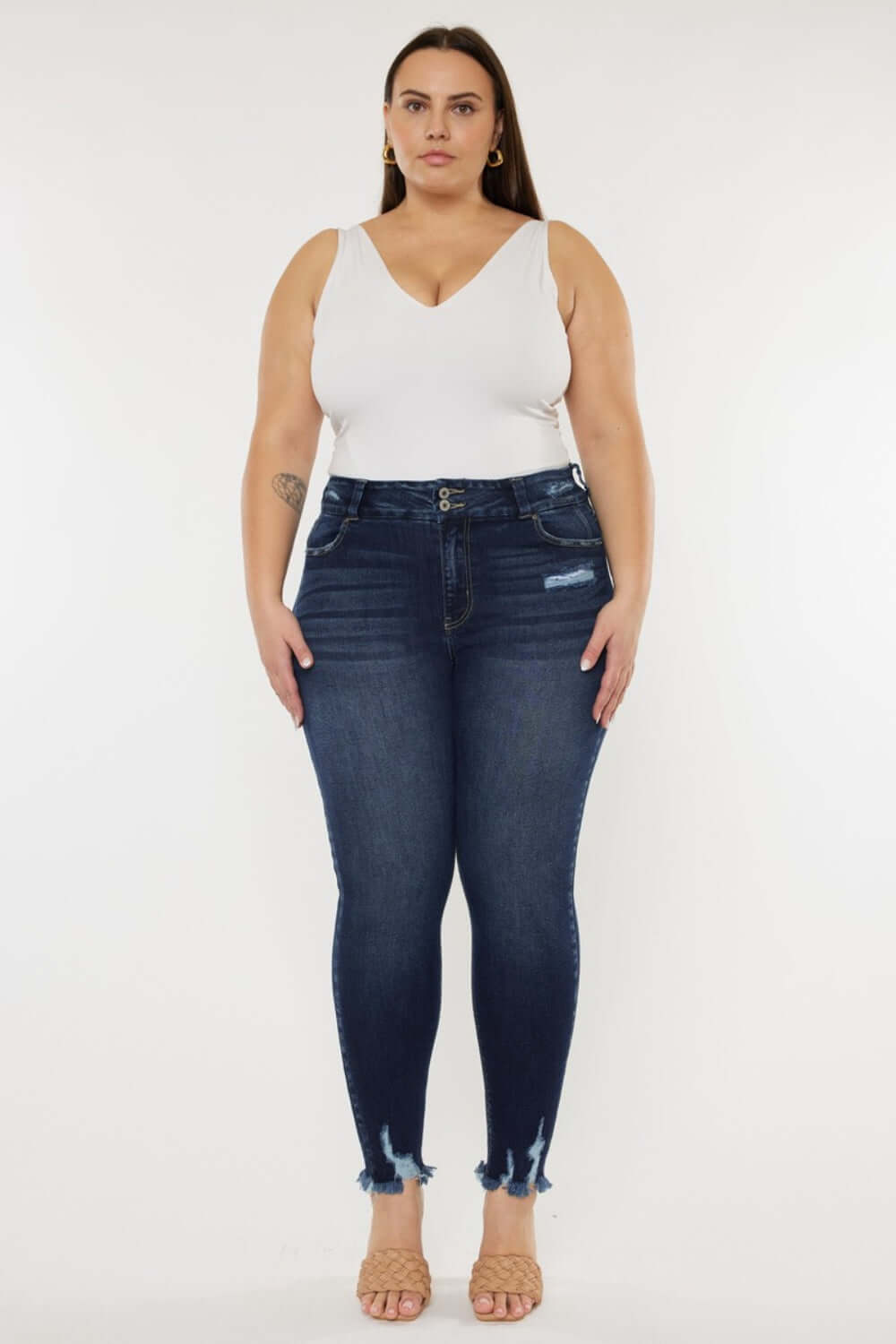 Woman wearing high waist jeans with raw hem detailing and a white sleeveless top, showcasing a chic and edgy fashion style.