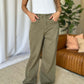 Woman wearing RFM Full Size High Rise Garment Dye Wide Leg Jeans in olive green with white tank top and sneakers.