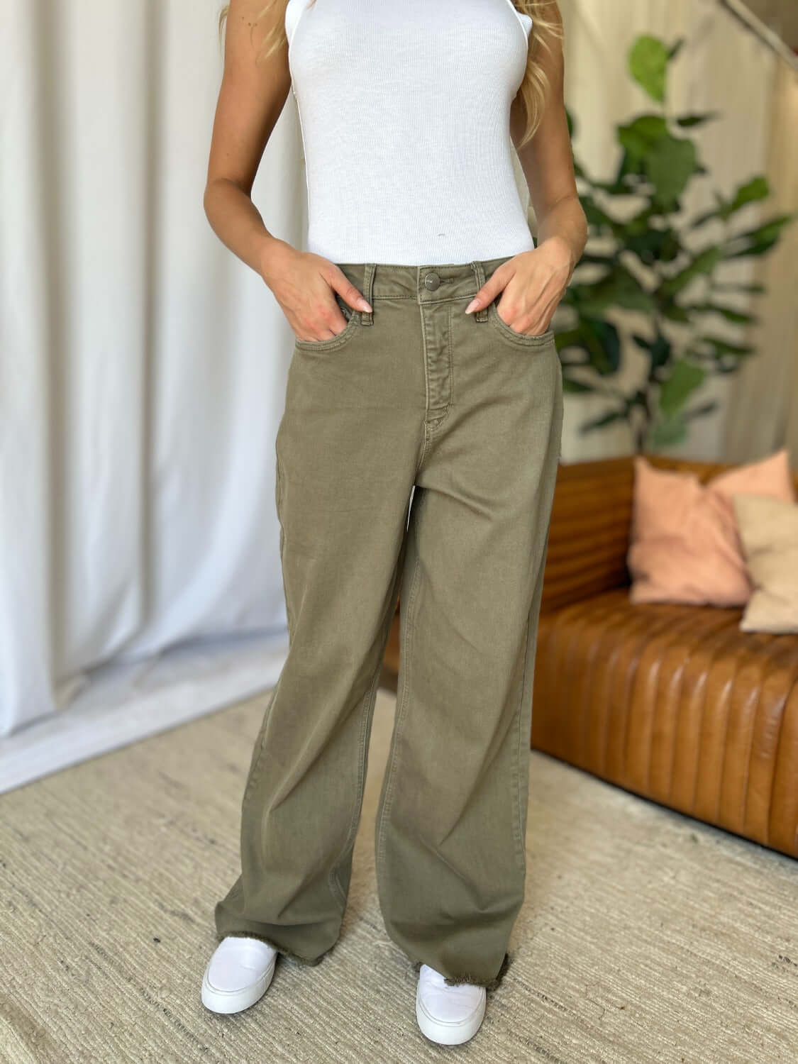 Woman wearing RFM Full Size High Rise Garment Dye Wide Leg Jeans in olive green with white tank top and sneakers.