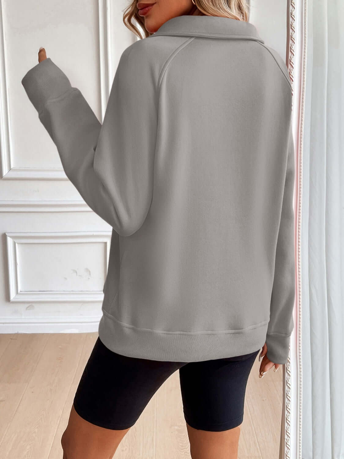 Ivy Lane Half Zip Raglan Sleeve Sweatshirt in grey, back view. 100% polyester, pocketed, opaque, machine washable. Model wearing black shorts.