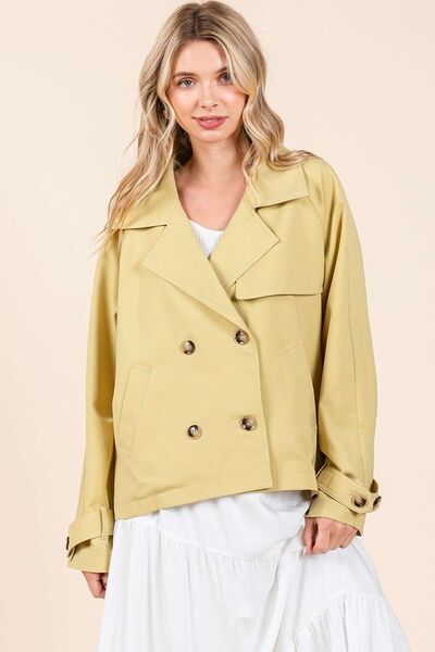 Elegant woman in yellow double-breasted trench coat, showcasing modern style and sophistication in a light outfit.