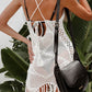 Woman wearing a white crochet tassel openwork spaghetti strap cover up dress with a black crossbody bag, standing outdoors near green foliage.