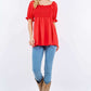 Woman wearing Ruffled Short Sleeve Smocked Blouse in red, paired with blue jeans, cowboy boots, and a hat for a stylish and comfortable look