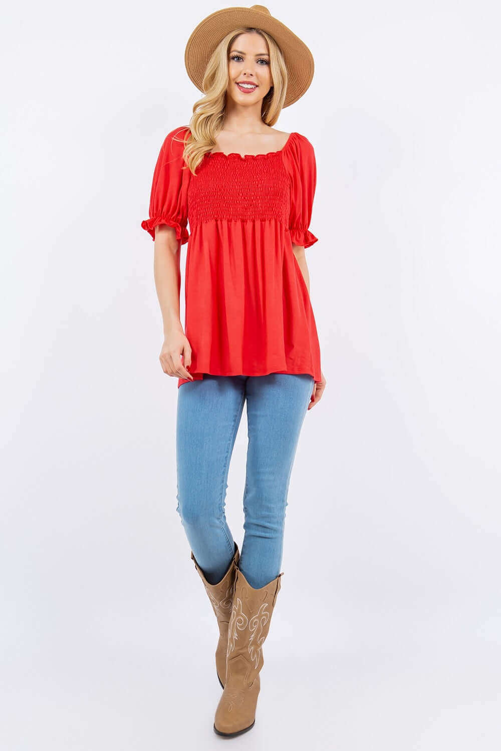 Woman wearing Ruffled Short Sleeve Smocked Blouse in red, paired with blue jeans, cowboy boots, and a hat for a stylish and comfortable look