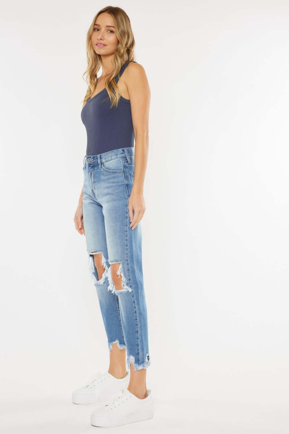 Model in High Waist Chewed Up Straight Mom Jeans with frayed edges and distressed holes, pairing them with a navy tank top and white sneakers.