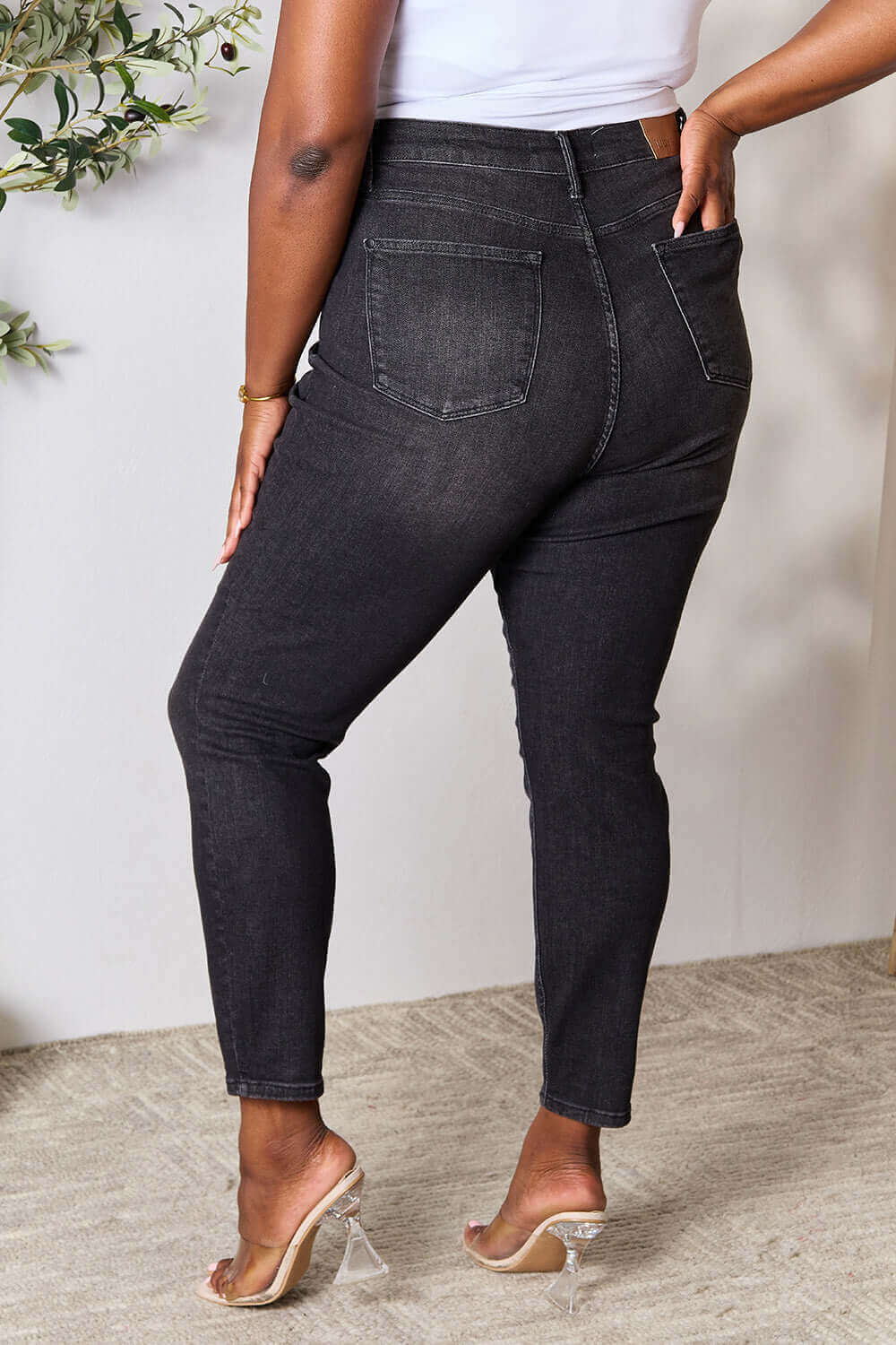 Woman wearing Judy Blue tummy control high waist denim jeans in black, showcasing back pockets and slightly stretchy fit. Full size.