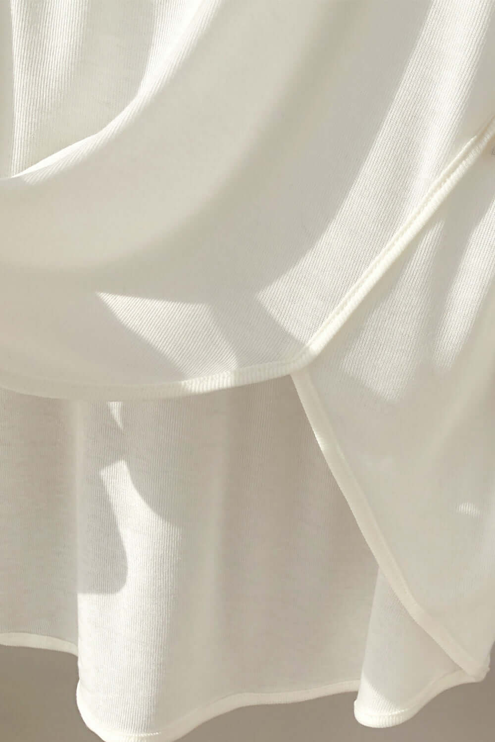 Close-up of Basic Bae High-Low Long Sleeve T-Shirt in white, showcasing the sheer fabric and stylish high-low hem detail.