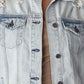 Close-up of distressed button-up denim jacket by Risen Jeans with fraying and worn-in details.