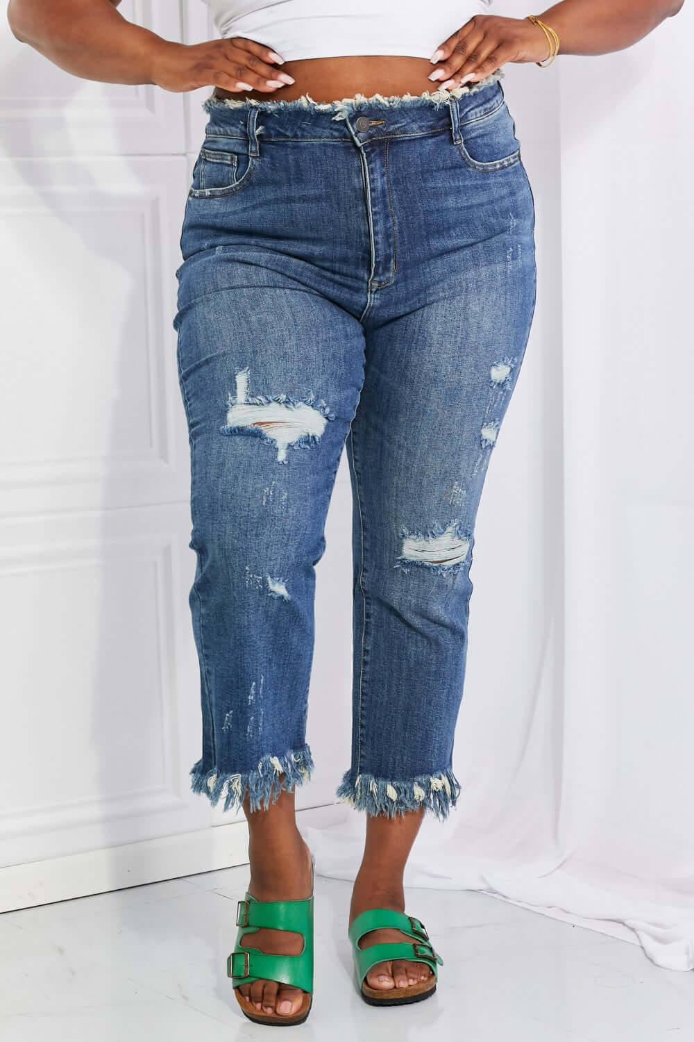 Woman wearing Undone Chic Straight Leg Risen Jeans with distressed details, raw hem, and high-waist, paired with a crop top and green sandals