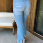 Woman wearing Bella Road distressed raw hem jeans with pockets standing by wooden wall and white chair