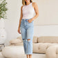 Woman wearing Tummy Control High Waist Raw Hem Distressed Jeans | Petite by RFM Jeans in a modern living room