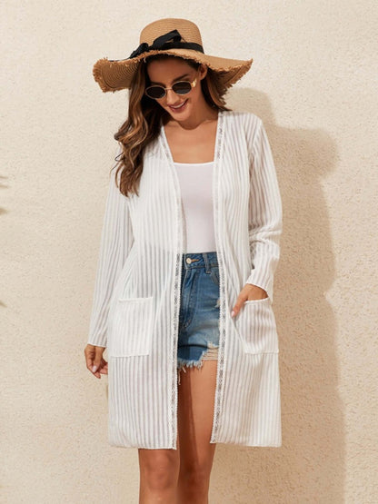 Woman wearing a lace detail open front long sleeve cover-up paired with denim shorts and a sun hat.