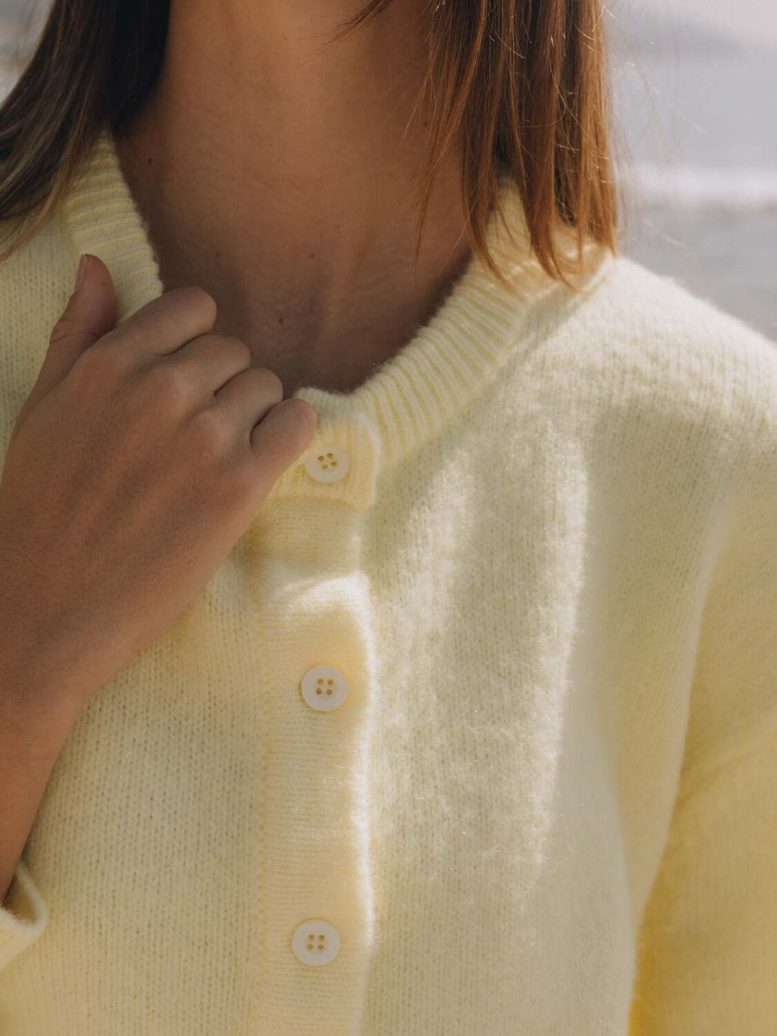 Close-up of a woman in a pastel yellow Bella Road Button Down Cardigan with button details, perfect for cozy days.