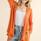 Woman wearing orange thermal hooded open front cardigan with pockets, styled with a white tank top and ripped jeans, looking cozy and fashionable