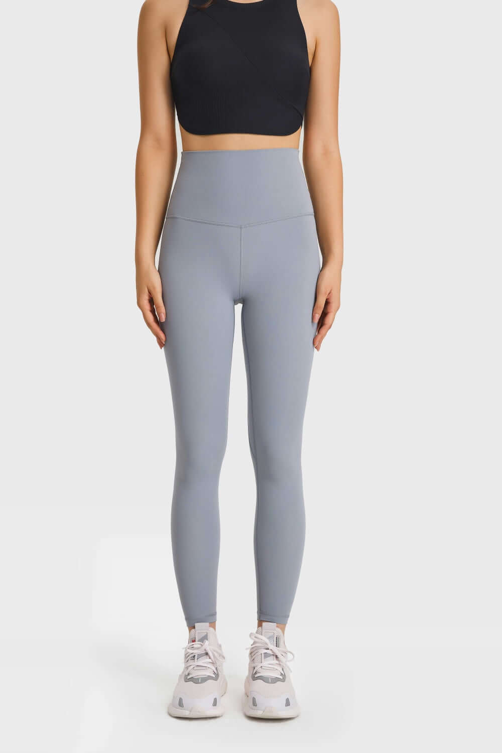 Woman in high waist grey leggings and black crop top, showcasing athleisure style for yoga or casual wear.