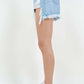 Side view of woman wearing high waist fringed hem denim shorts paired with white sneakers.